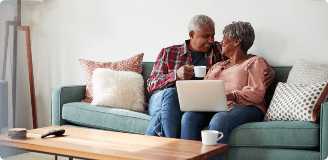 Senior Couple Sitting On Sofa At Home Using Laptop To Shop Online